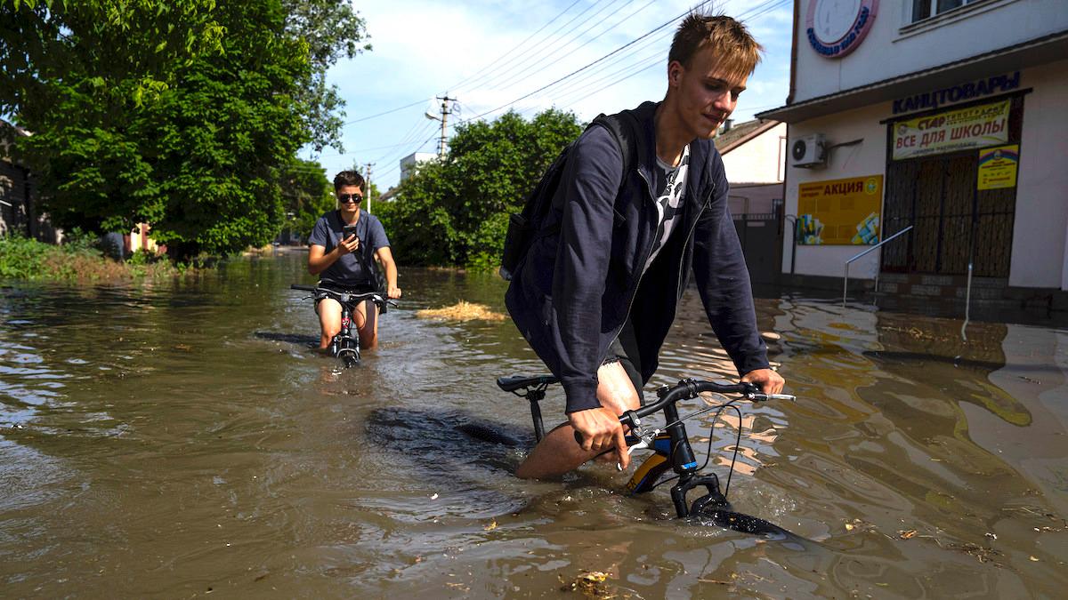 Lokalbor försöker cykla längs en översvämmad väg efter att Nova Kakhovka-dammen brast natten till tisdag