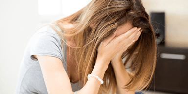 Kvinna med händerna för ansiktet, symbol för hur rikedom och sparande kan påverka relationer och livskvalitet negativt.