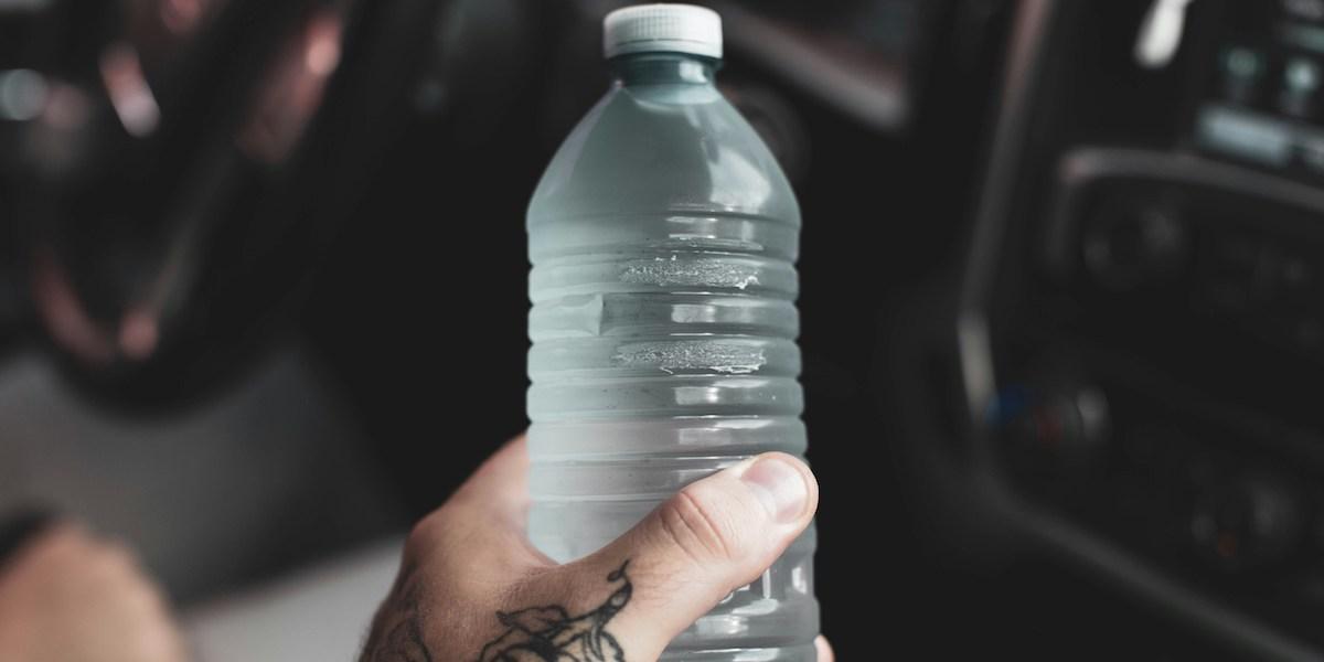 Hand som håller plastflaska fylld med vatten.