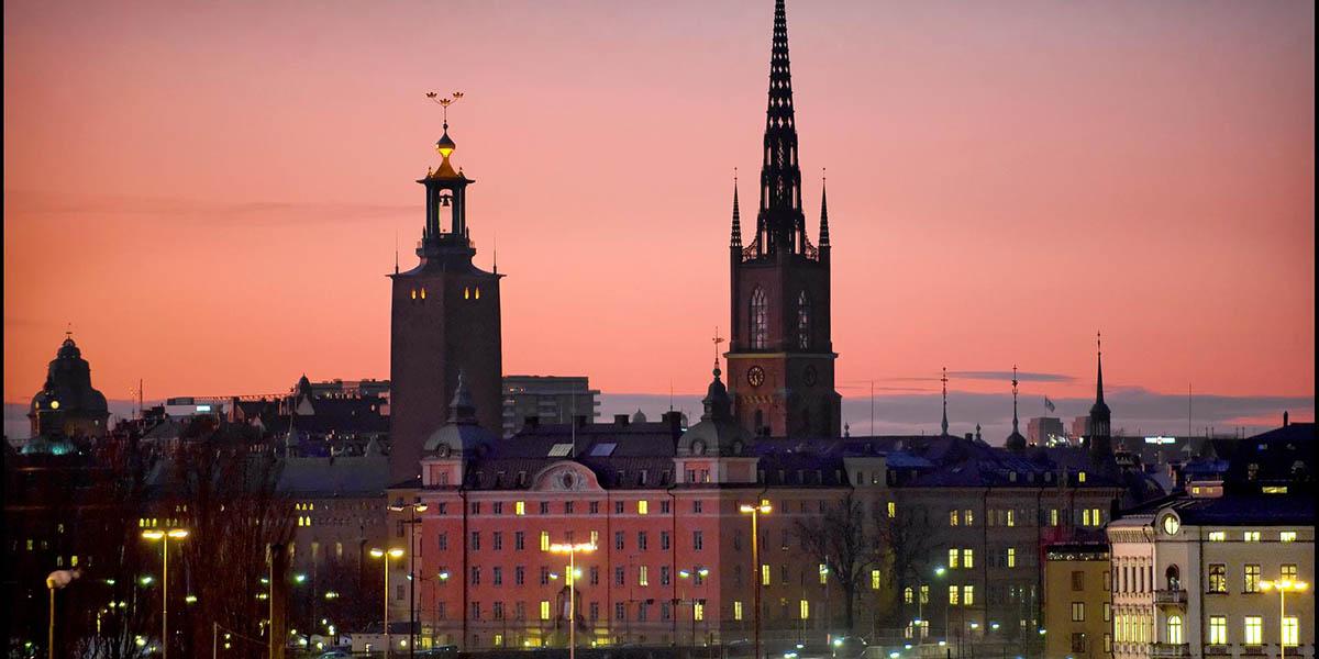 En kvällsbild över stockholm där silhuetterna av Riddarholmskyrkan och Stadshuset syns.