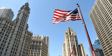 Amerikansk flagga framför höga byggnader i finansdistrikt – inflation och räntor i fokus i USA.